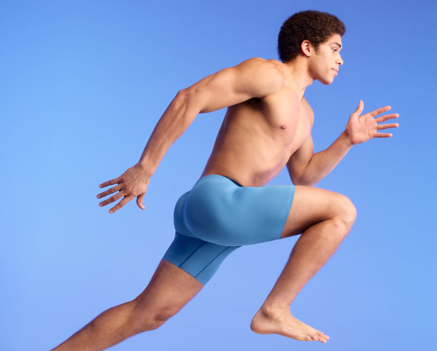 Man wearing light blue athletic shorts against a blue background