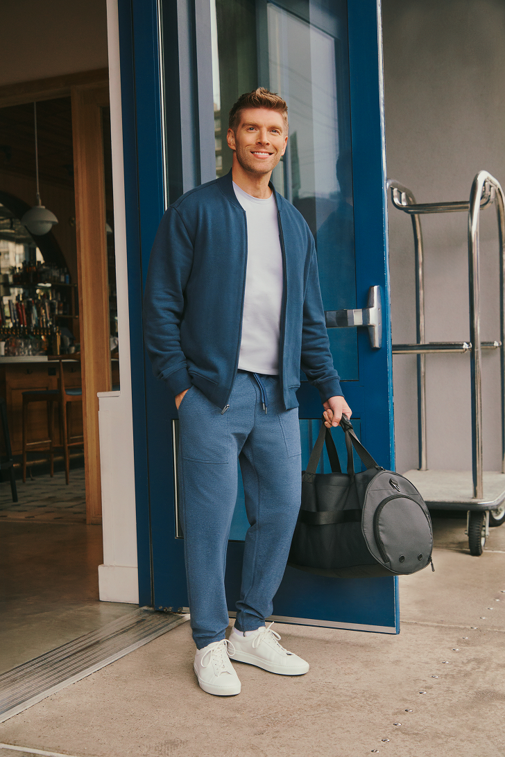 Man in blue outfit holding a duffel bag outside a building